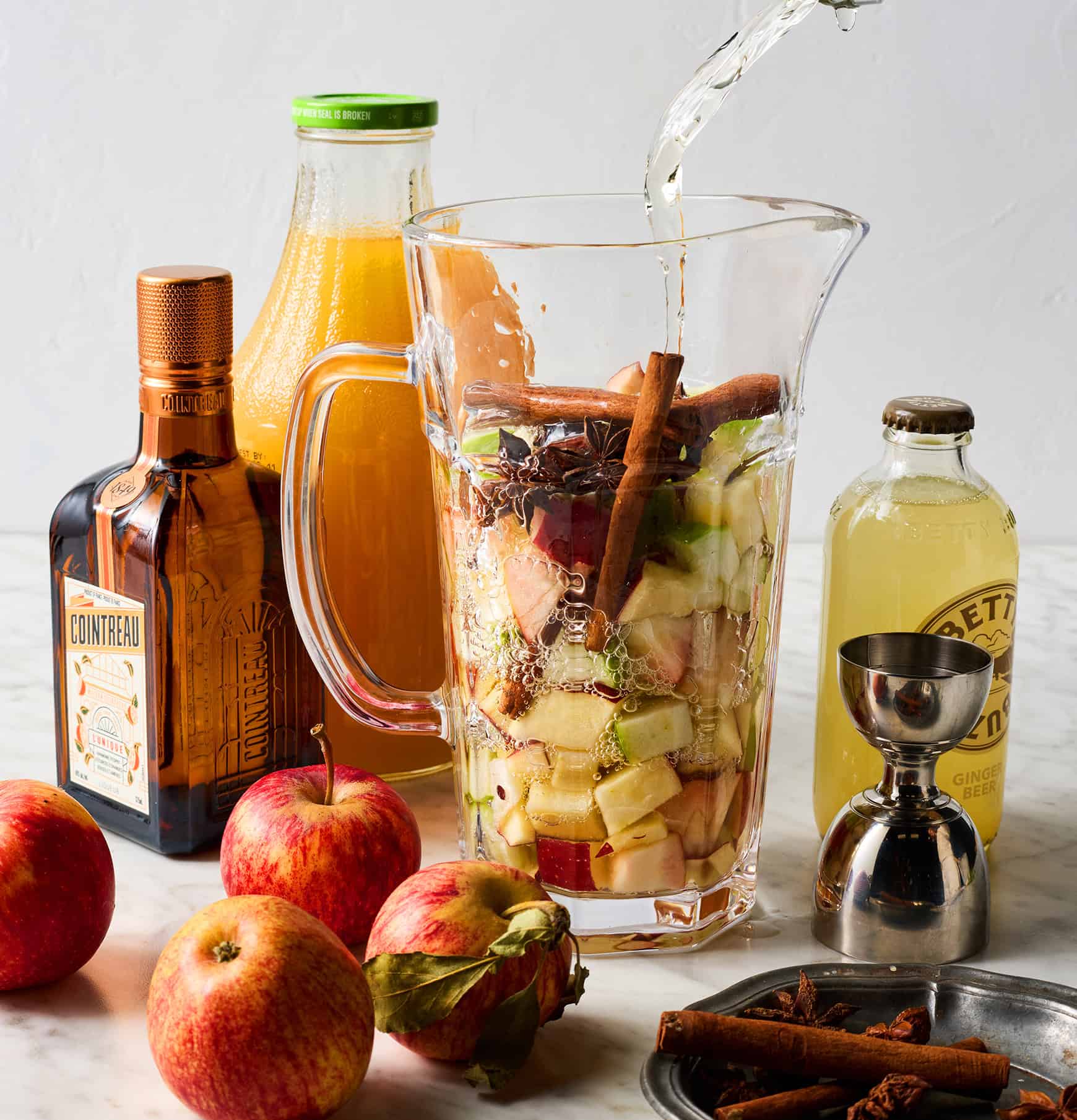 Pouring white wine into pitcher with apples and spices