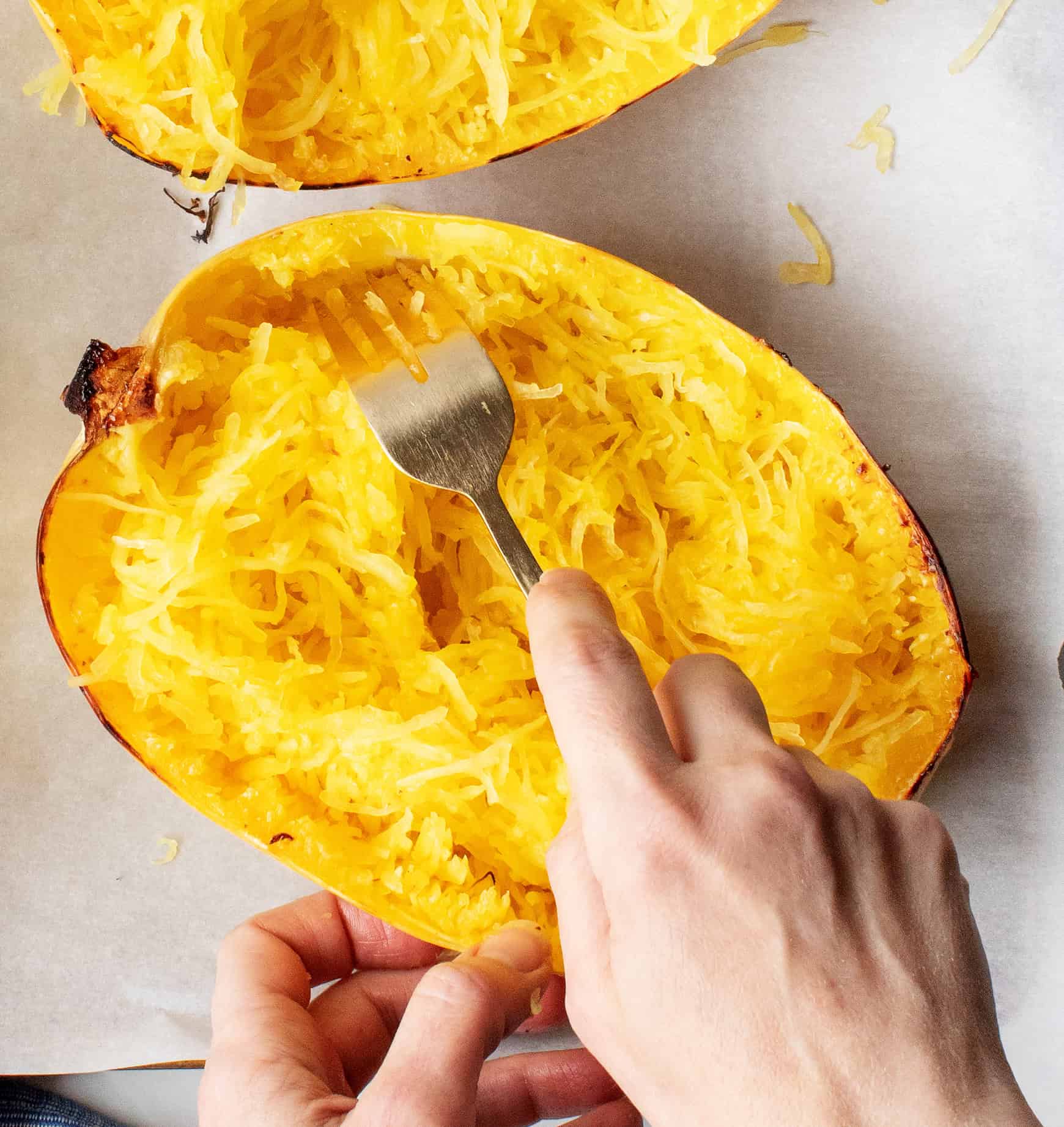 Hands fluffing spaghetti squash with a fork
