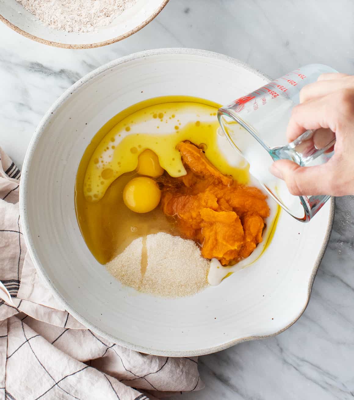 Hand pouring milk into bowl of wet ingredients for pumpkin bread recipe