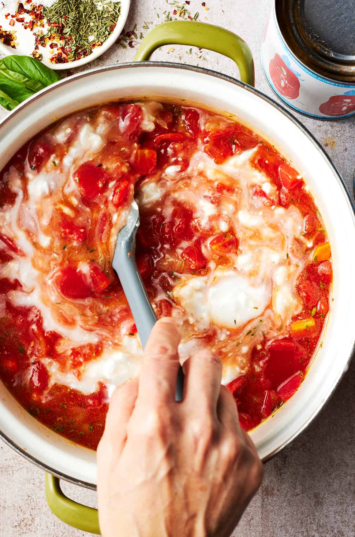 Hand using spatula to stir cream into pot of homemade tomato soup