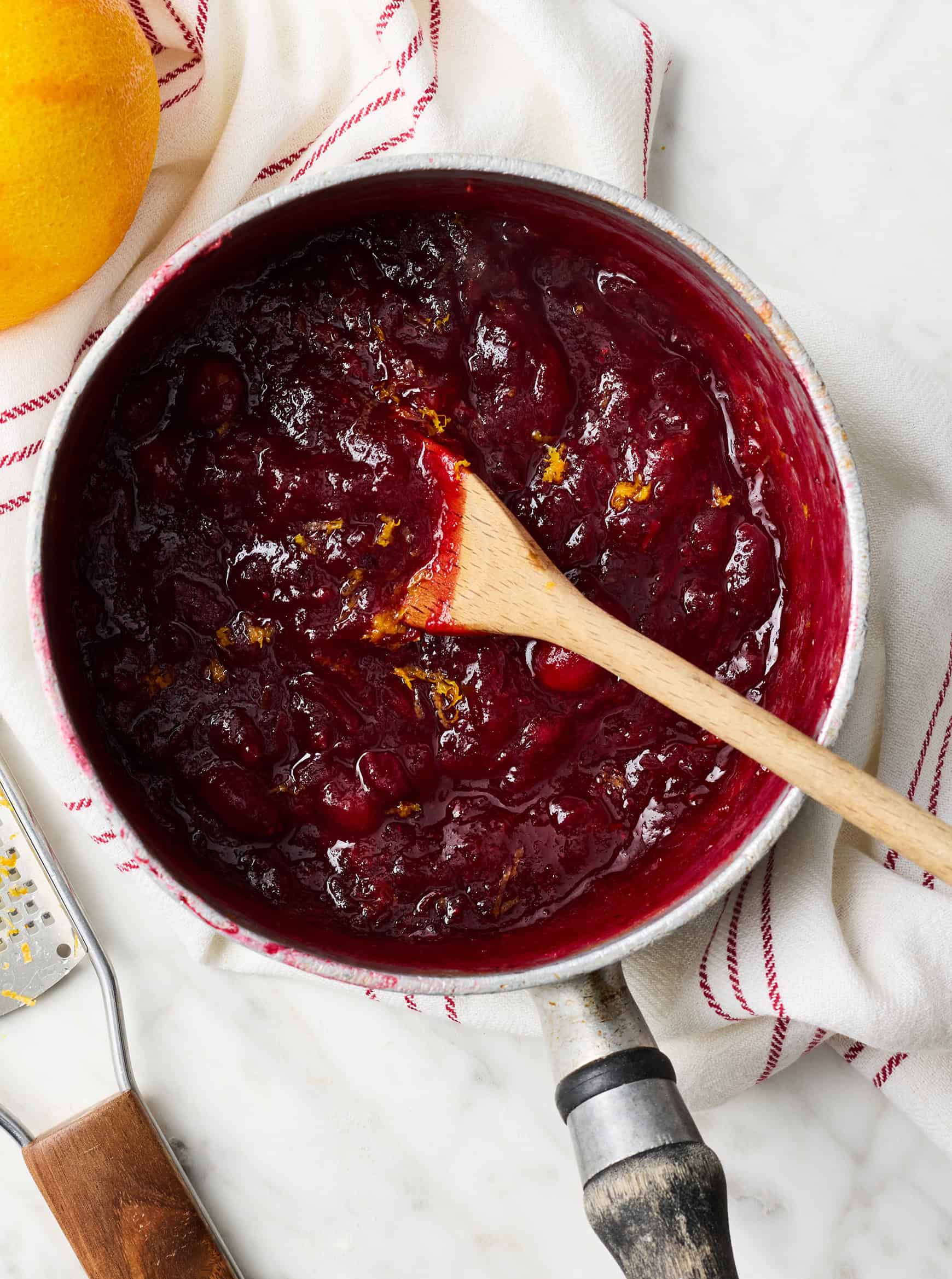 Adding orange zest to cranberry sauce in saucepan