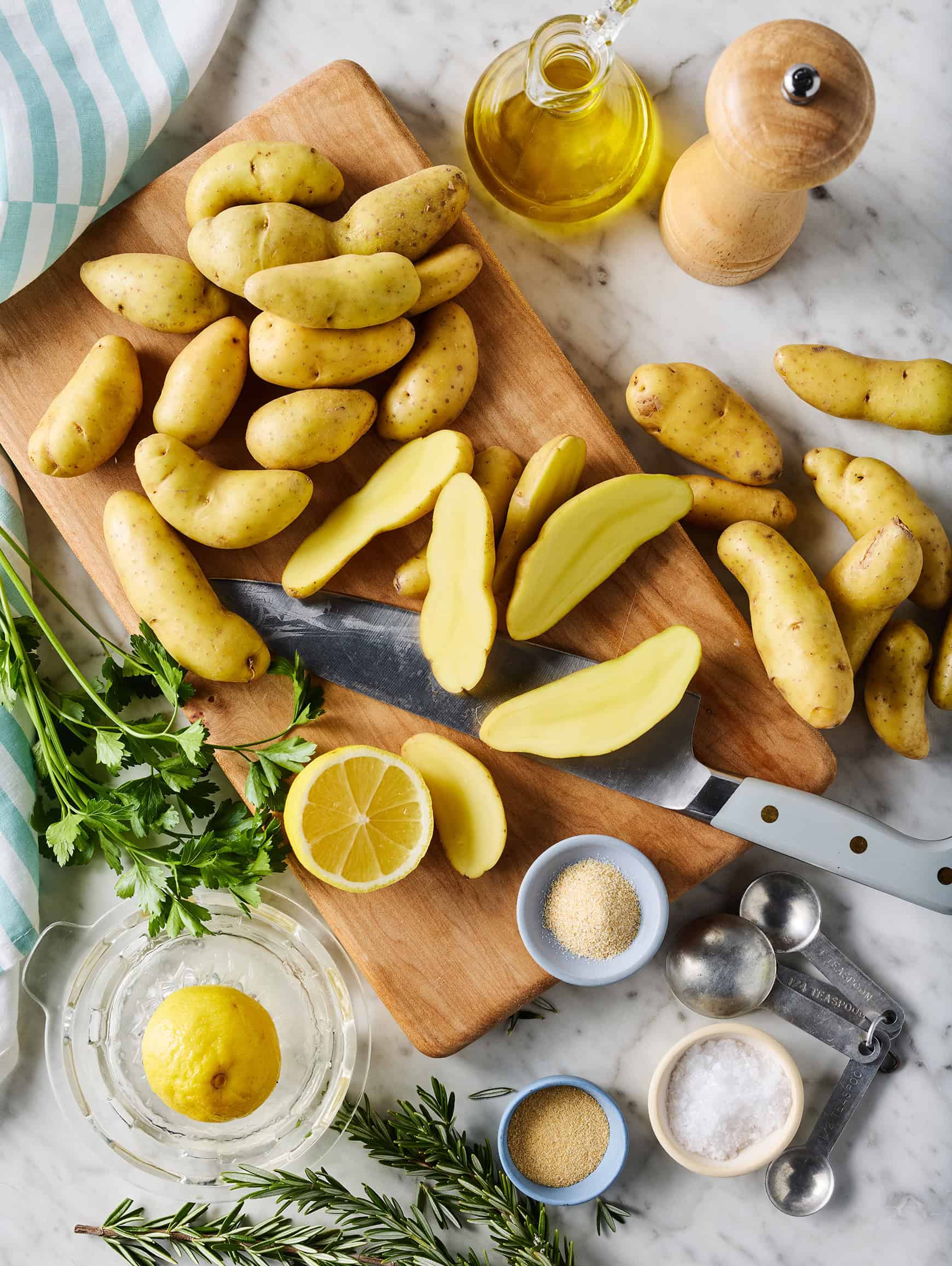 Halved fingerling potatoes on cutting board with lemon, parsley, and seasonings