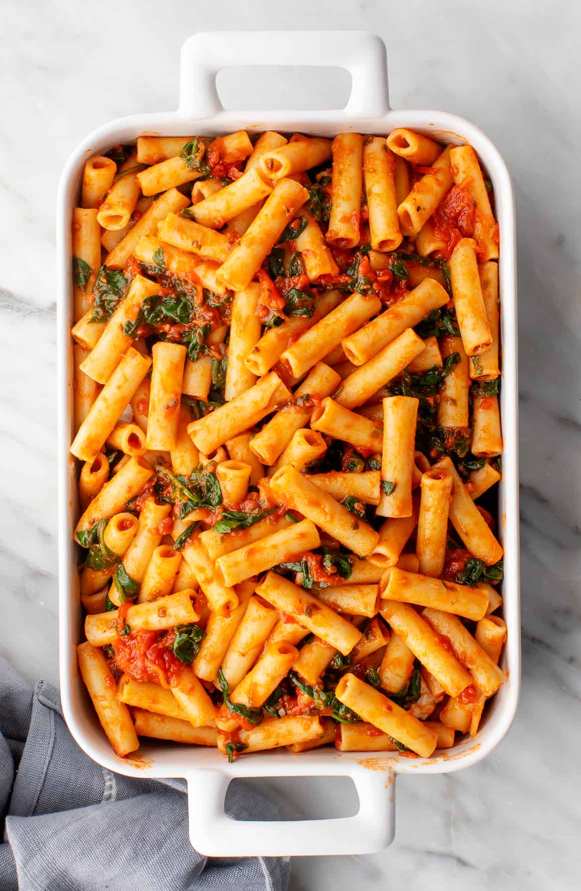 Pasta with marinara sauce and sautéed spinach in a baking dish