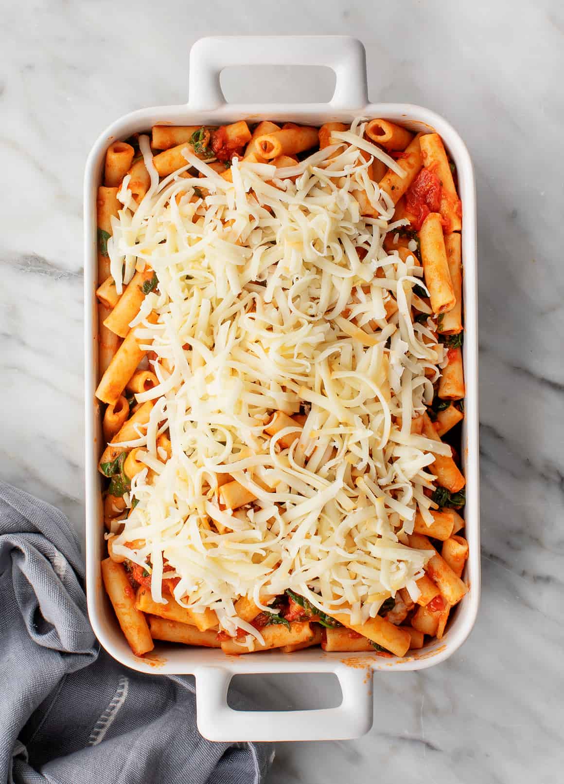 Saucy ziti pasta in a baking dish topped with grated cheese