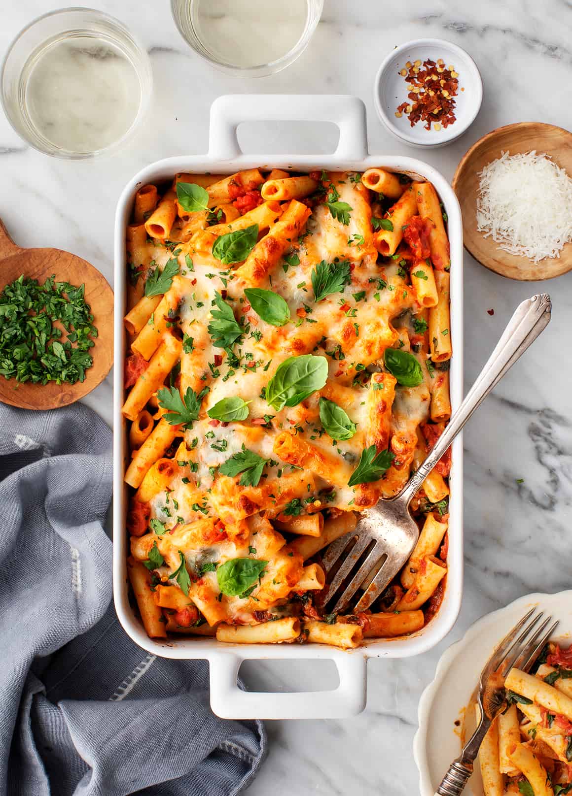 Easy baked ziti in a baking dish topped with basil and chopped parsley