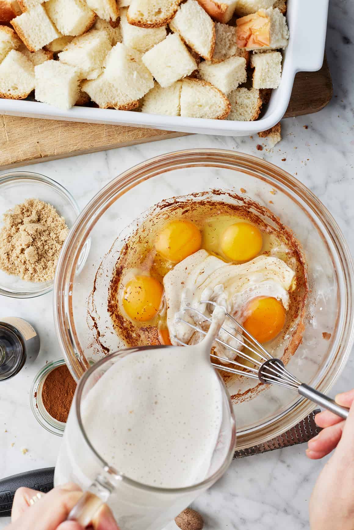 Hand whisking together milk, eggs, cinnamon, and nutmeg in a large bowl