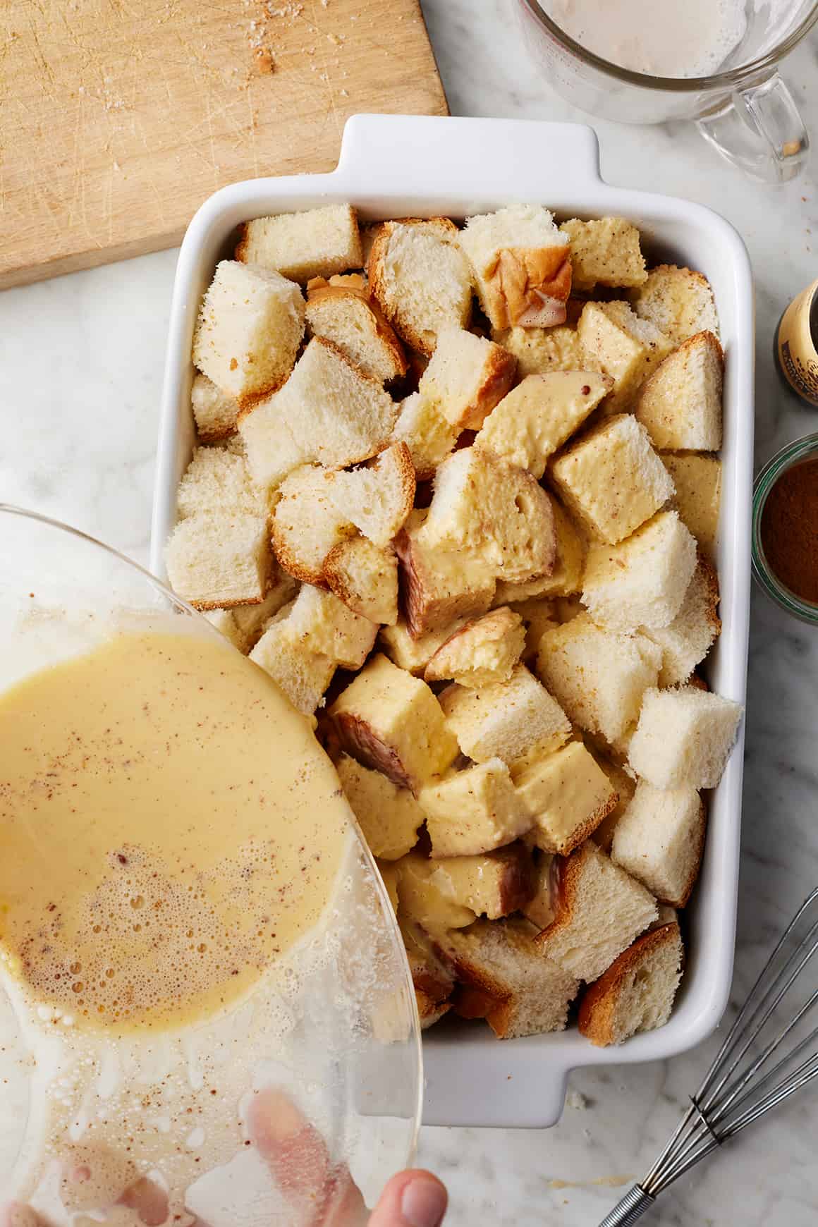 Pouring egg mixture over bread cubes in baking dish
