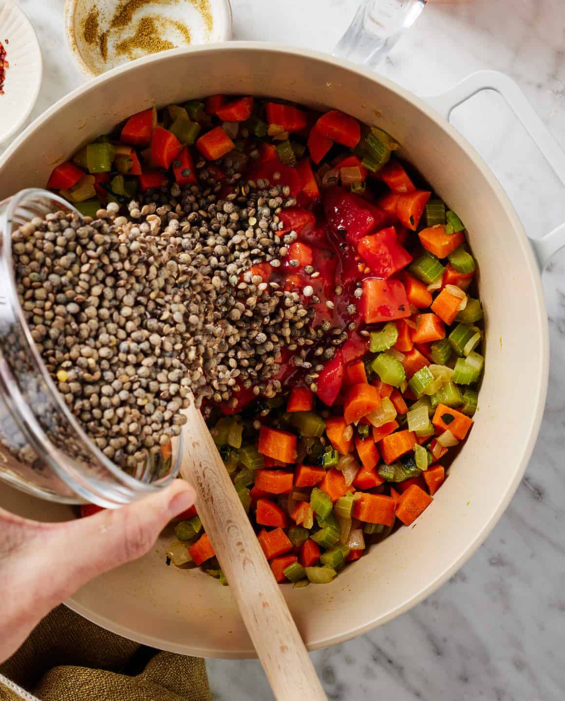 Adding lentils to soup pot with vegetables