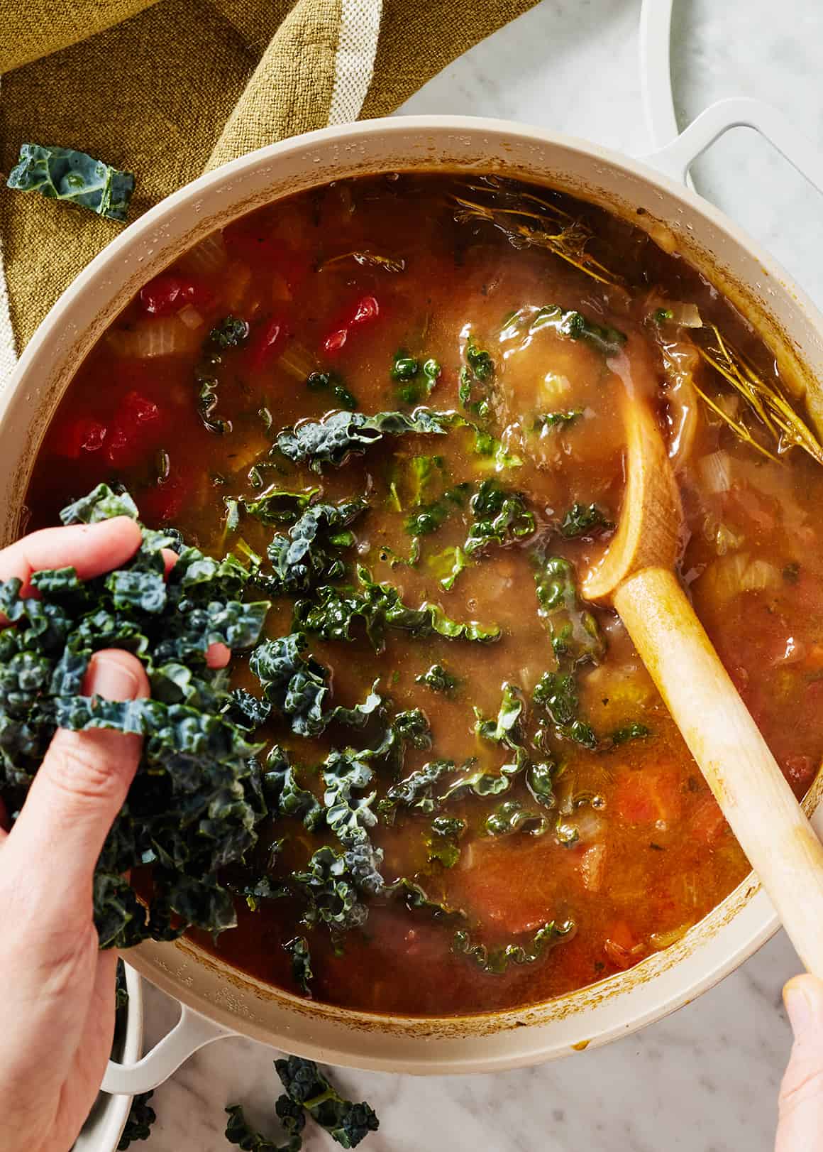 Stirring kale leaves into pot of lentil soup