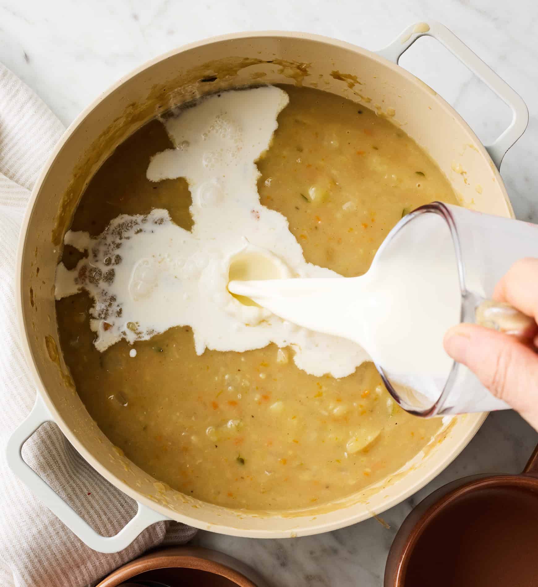 Pouring cream into pot of potato soup